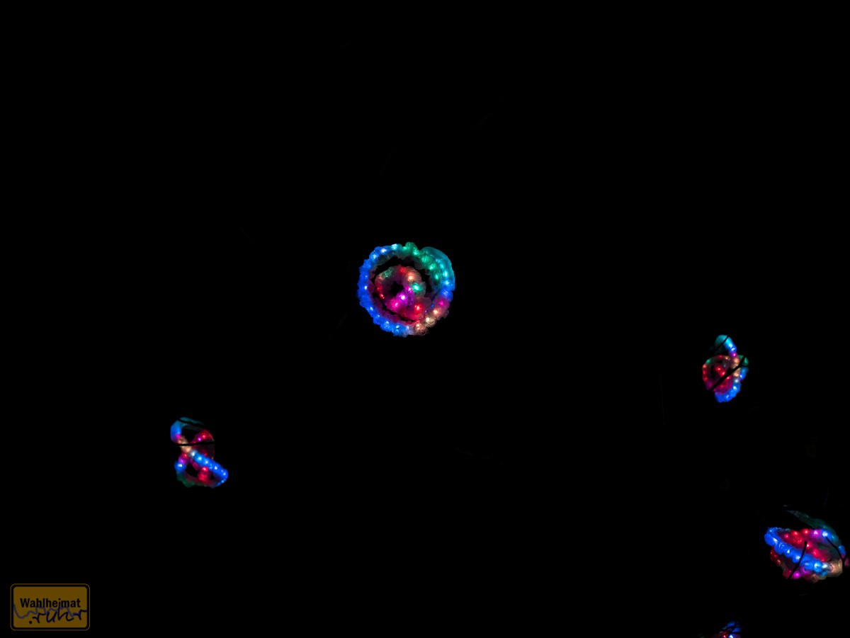 In der Kastanienallee leuchten "Lumi-Seeds" auf - in den Bäumen hängen farbige Luftschlangen in fluoreszierenden Farben.